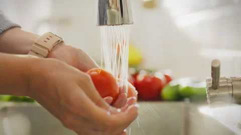 In the kitchen sink, a woman's hands carefully wash tomatoes under running w Stock Footage 283686004