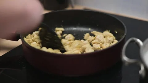 In a kitchen, small pieces of chicken are being cooked in a pan on a stove. A Stock Footage 338298538