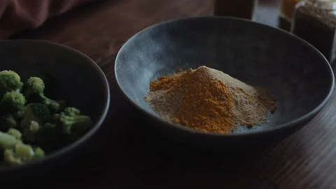 On the kitchen table are bowls with a mixture of spices and broccoli for Stock Footage 127568096