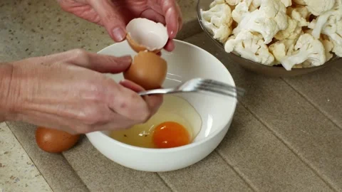 On the kitchen table, in the foreground, a woman's hands are breaking eggs with Stock Footage 220695686