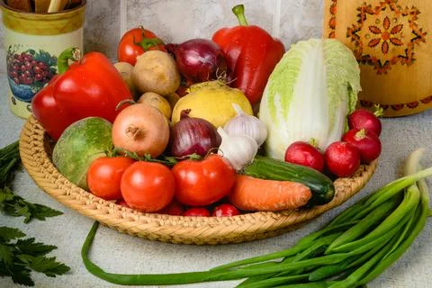 On the kitchen table, in the large wicker basket are a variety of vegetables. Stock Photos