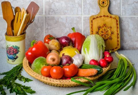 On the kitchen table, in the large wicker basket are a variety of vegetables. Stock Photos