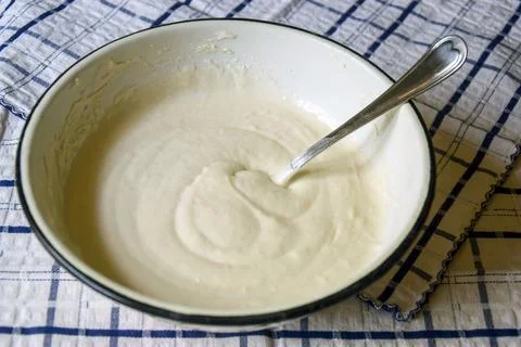 On kitchen table there is an enameled bowl with spoon and liquid dough Stock-Fotos