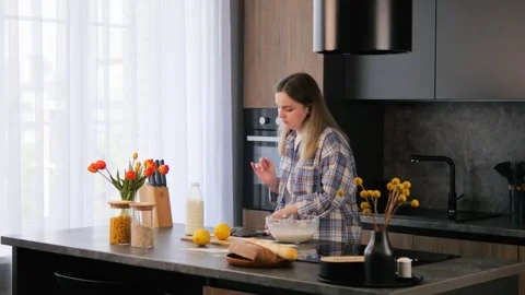 On kitchen table, woman beats eggs in bowl to prepare delicious omelette for Stock Footage 277399963