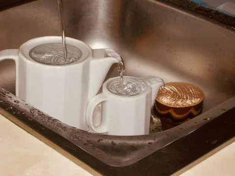 Kitchen teapots being filled incorrectly with water in a sink Foto stock
