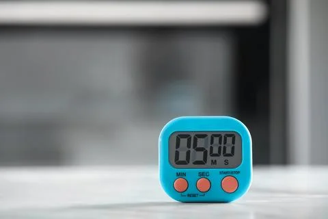 Kitchen timer on light grey table against blurred background. Space for text Stock Photos