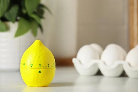 Kitchen timer in shape of lemon and eggs on white table. Space for text Stock Photos