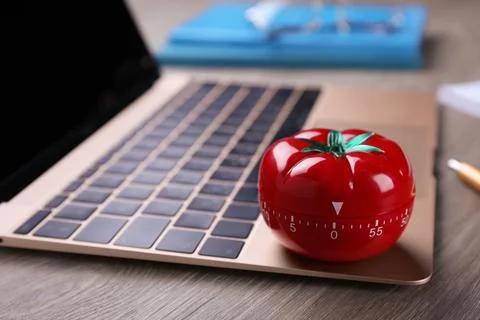Kitchen timer in shape of tomato and laptop on wooden table, closeup. Space.. Stock Photos