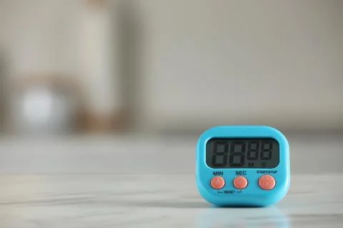 Kitchen timer on white marble table against blurred background. Space for tex Stock Photos