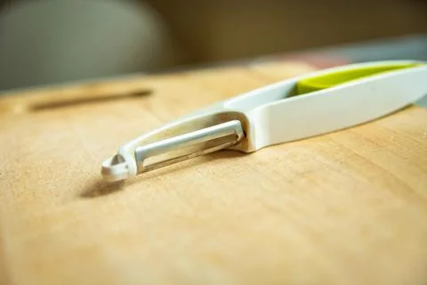 A kitchen tool for peeling vegetables is lying on a wooden board Stock Photos