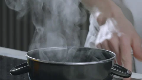 Kitchen work A cook removes a steaming pot from an electric stove. Boiling water Stock Footage 266819421
