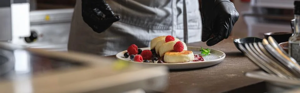 Kitchen worker decorated ready cheesecakes with berries for breakfast in Stock Photos