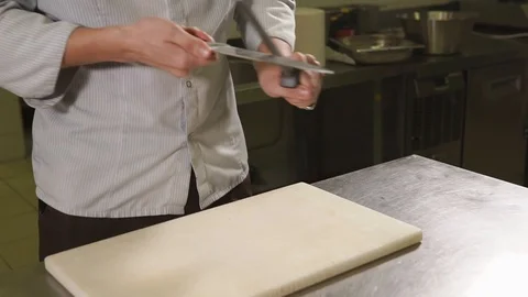 Kitchen worker man is sharpening a knife, standing near kitchen table Stock Footage 86660541