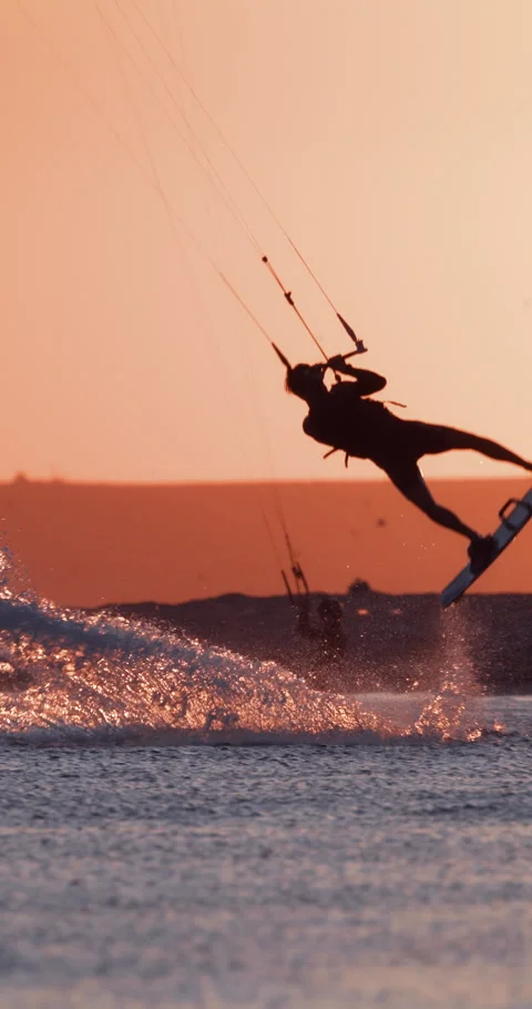 Kite boarder riding and jumping high above the sea with kite against a sunset Stock Footage 345128720