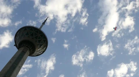 A kite with the flag of Iran flying close to the Milad Tower - Tehran Tower Stock Footage 66542333