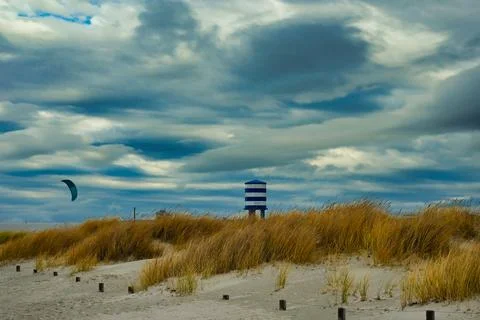 Kite surfer near sandy beach with grass and a striped lifeguard tower under.. Stock Photos