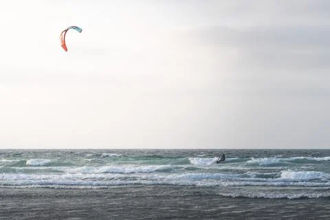 Kite surfer rides the waves at dawn on a coastline near mountains 写真素材
