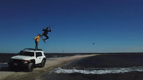 A kitesurfer doing a high five to a man standing on the car, aerial shot 스톡 동영상 112657437
