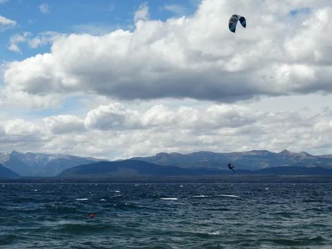 Kitesurfer performing jump trick over lake by mountains Stock Photos