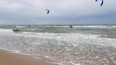 Kitesurfers riding waves in the ocean on a cloudy day Stock Footage 320723942