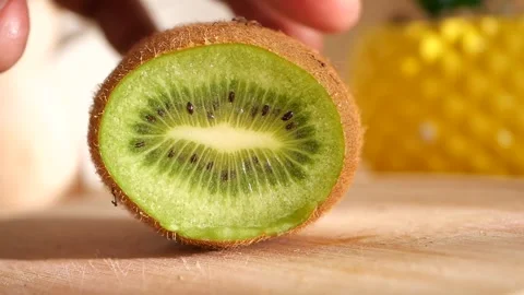 Kiwi fruit slice being cut with sharp metal knife on wooden board in bright.. Stock Footage 332745188
