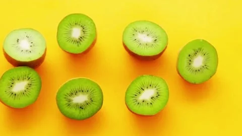 Kiwi halves rotating on bright yellow surface in top view stop motion. Video stock 336331508