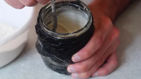 Kneading liquid yeast-free starter in a glass jar shaded with a black bag Stock Footage 276478913