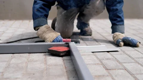 Kneeling worker uses handheld metal cutting tool on gray support over brick Stock Footage 344872689