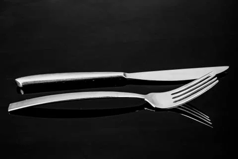 Knife and fork with mirroring only the head with tines in silver metallic Stock Photos