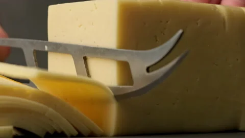 Knife cuts cheese into slices. Close-up shot of piece of delicious cheese. Video stock 204027628