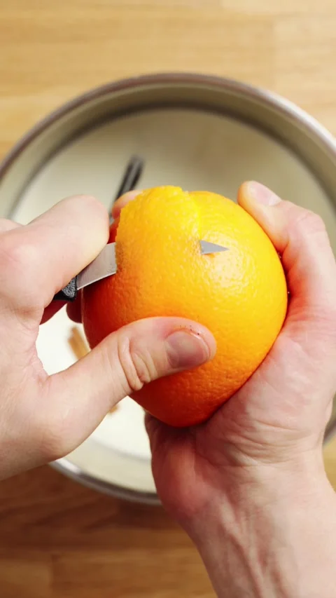 Knife cuts orange peel and drops it into milk mixture. Stock Footage 345273860
