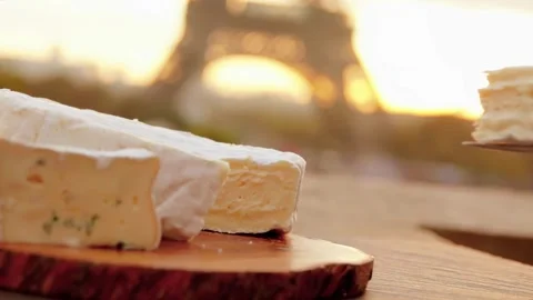 A knife cuts a slice of soft cheese against of the sunrise over the Eiffel Tower Vídeo Stock 303423334