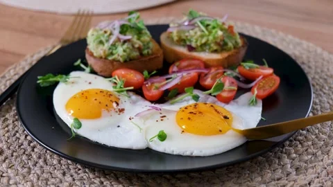 Knife cutting fried egg with runny yolk flowing over avocado toast Vídeos de archivo 332751659