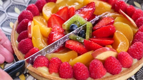 A knife is cutting a fruit pie with strawberries, kiwi, and raspberries Stock Footage 284913497