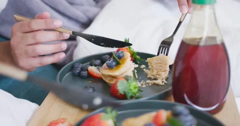 Knife is cutting pancakes on plate on bed tray as fork is lifting bite for Stock Footage 344402196