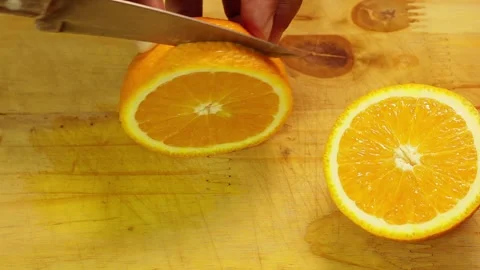 Knife cutting slices of fresh orange on a wooden board in a diner kitchen 動画素材 338337156