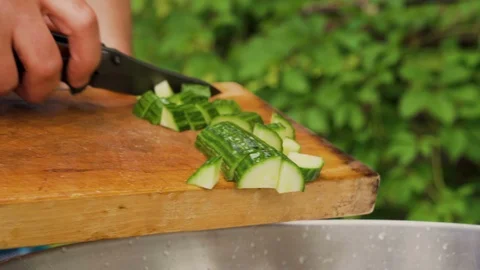 Knife pushes cut pieces of cucumber from wooden board to metal bowl,outdoors Stock-Footage 111648327