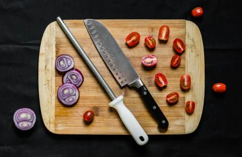 A knife sharpener and a chef knife on a cutting board with vegetables Stock Photos