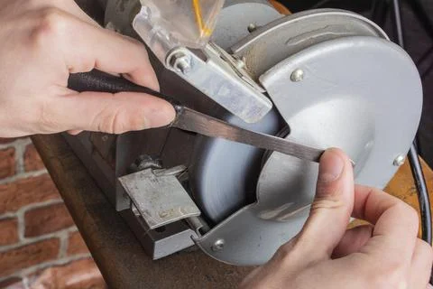 Knife sharpener and hand with blade on wooden table, closeup Stock Photos