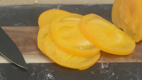 A Knife skillfully slicing through a ripe, yellow tomato on a wooden cutting Vidéo 280113114