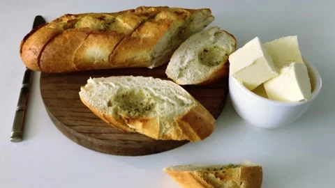 Knife-sliced white garlic bread on a wooden board with chunks of butter Stock Footage 196603764