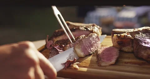 Knife slicing a grilled steak held by a carving fork on a wooden cutting board Stock Footage 339977505
