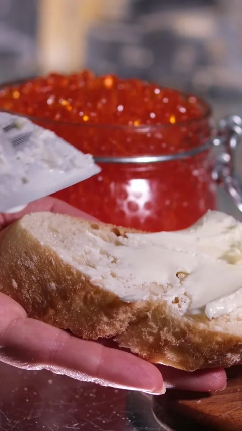 With a knife to spread butter on bread in the background a glass jar with caviar Stock Footage 252151702