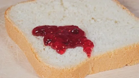 Knife spreads red fruit jam on piece of white bread with golden crispy crust on Stockbeeldmateriaal 196268969
