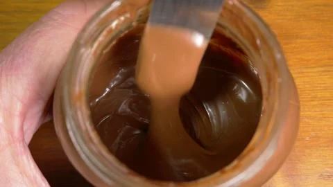 A knife stirring chocolate hazelnut spread in a jar. Stock Footage 264107069