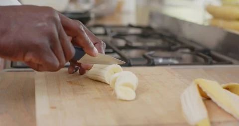 Knife tip touching banana hands are making short downward cuts producing slices Vidéo 339272379
