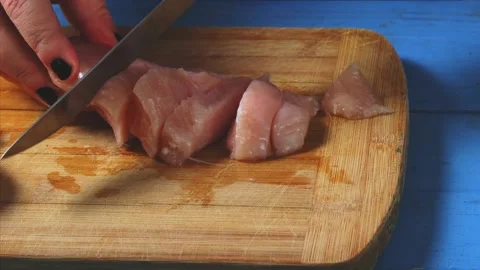 A knife in a woman's hand cuts a chicken breast on a cutting board. Close-up. Video stock 305405146