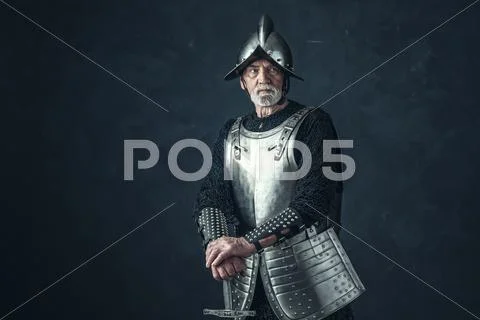 Knight in armor with gray beard holding sword. Stock Photos