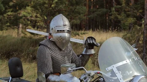 Knight in full armor sits on a motorcycle against the backdrop of the forest. Stock Footage 156469426