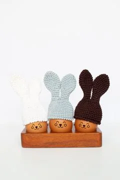 Knitted Easter eggs with bunny ears hats in a wooden stand on a white table. Stock Photos